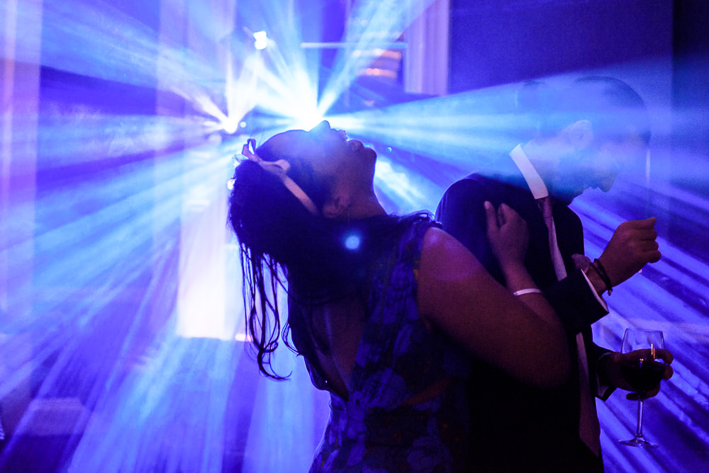 Image of a lady throwing her head back and laughing at a wedding reception with DJ lighting in the background.