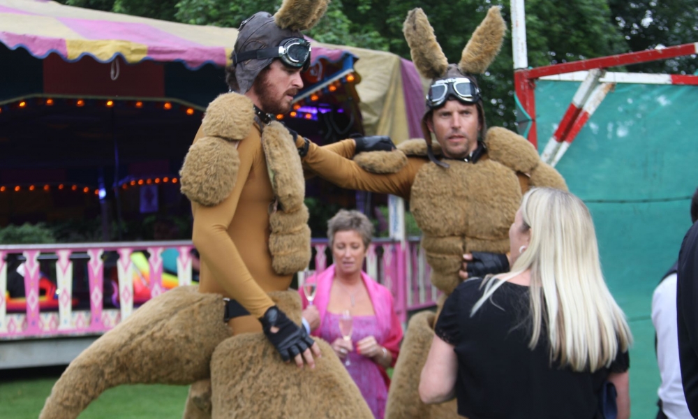 Image of a lady talking to giant Kangaroos with Dodgems in the background.