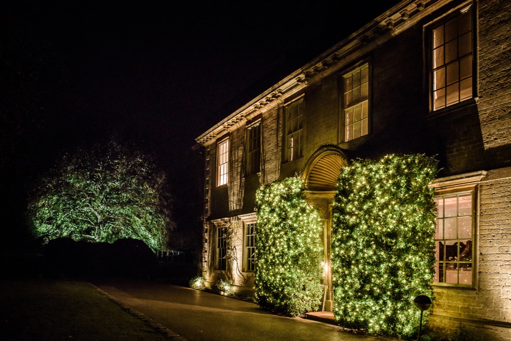 Exterior of Babington House Hotel with wedding lighting in bushes.
